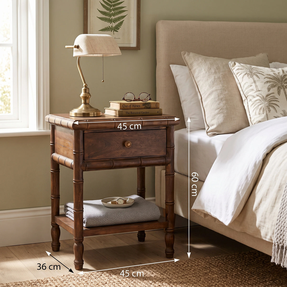 A dark brown bamboo-style nightstand in a bedroom setting, styled with a brass table lamp, books, and glasses, positioned next to a bed with neutral-colored bedding. height: 60 cm, width: 45 cm, depth: 36 cm.