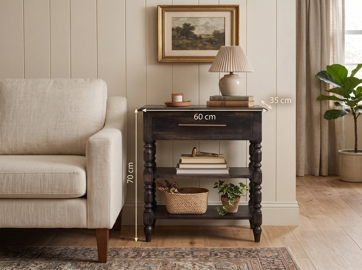 A solid mango wood 1-drawer turned-leg side table in a dark carbon ash finish, styled in a living room next to a light beige sofa with a lamp and decor on top. White dimension lines and text indicate the table's height as 70 cm, width as 60 cm, and the lamp top depth as 35 cm.