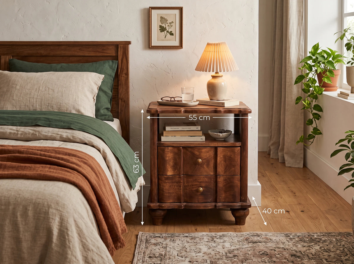 A solid mango wood 2-drawer bedside table with an open shelf in a roasted almond finish, styled in a bedroom next to a bed with green bedding. Dimensions overlay shows 55 cm width, 40 cm depth, and 63 cm height.