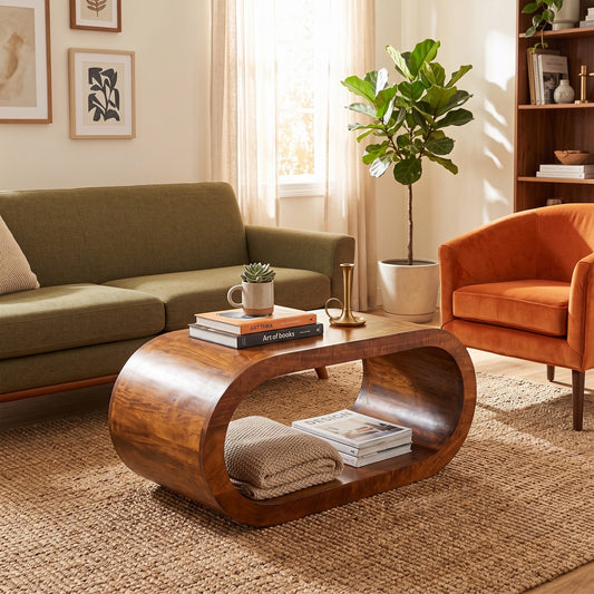 A modern curved wooden coffee table with a glossy finish, styled in a warm, sunlit living room next to an olive green sofa and an orange armchair.