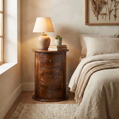 Wooden nightstand with lamp and books next to a bed in a bedroom.