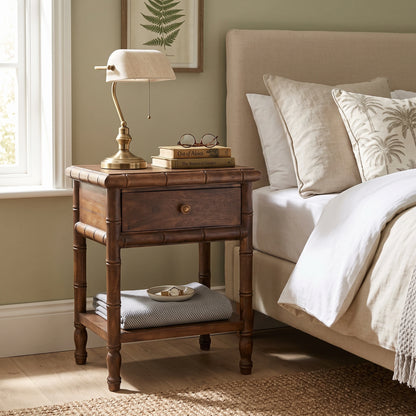 A dark brown bamboo-style nightstand in a bedroom setting, styled with a brass table lamp, books, and glasses, positioned next to a bed with neutral-colored bedding.