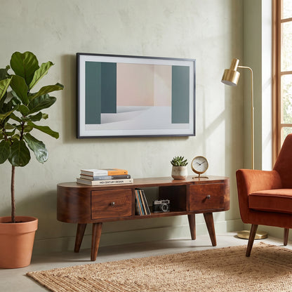 A framed abstract wall art print hangs above a dark wood media console in a styled living room. The artwork features a minimalist geometric design in muted teal, blush pink, cream, and white.