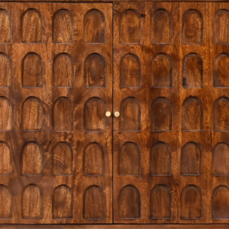 A close-up of a carved wooden cabinet door with two doors meeting at the center, featuring a repeating pattern of arched recessed panels and small round brass knobs.