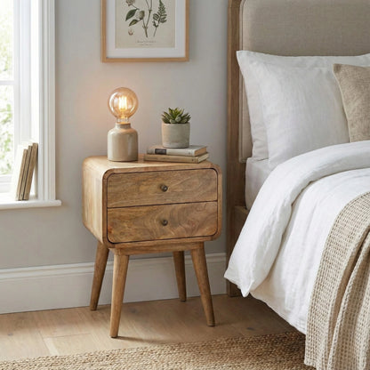 Wooden nightstand with lamp and plant next to a bed in a bedroom.