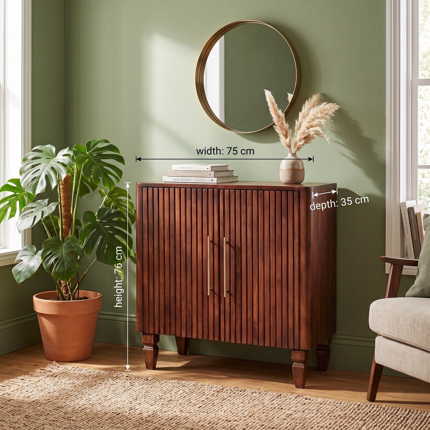 A wooden cabinet with two vertical slat doors and brass handles, shown in a styled room with wall measurements overlaid. The cabinet is brown wood with brass handles, set against a sage green wall next to a potted plant and a round mirror.