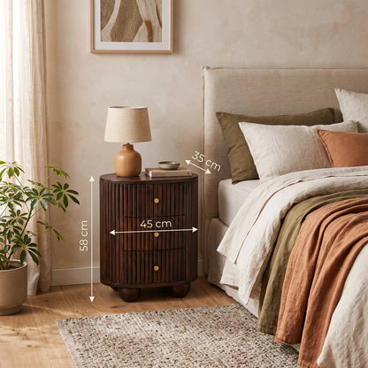 A fluted 3-drawer curved bedside table in solid mango wood with a velvet mocha finish, styled in a warm bedroom setting next to a bed with a small lamp on top. White dimension lines overlay the nightstand showing its height as 55 cm, width as 45 cm, and depth as 35 cm.