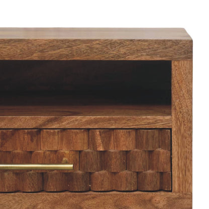 Close-up detail of the golden teak bedside table, highlighting the geometric carved wood texture on the drawer and the sleek brass bar handle.