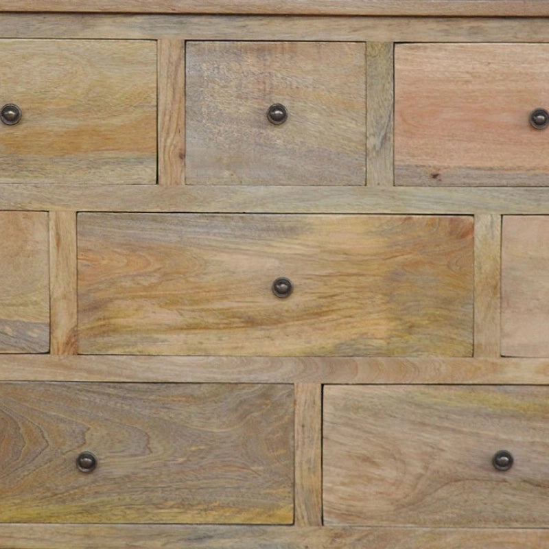 Close-up of a wooden chest of drawers with multiple rectangular drawers in natural light brown and beige wood tones, each fitted with a small round dark metal knob.