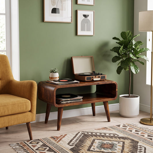 A mid-century modern wooden media unit styled in a living room setting with a mustard yellow armchair, a potted fiddle-leaf fig plant, a floor lamp, and a patterned rug against a sage green wall.