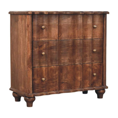 Angled left perspective of a solid mango wood chest in roasted almond, showcasing the wavy drawer panels, scalloped base, and bun feet.