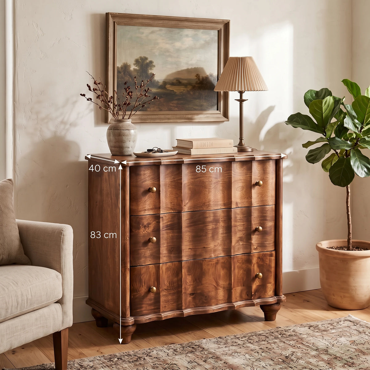 A panelled solid mango wood chest in a roasted almond finish, styled in a warm room setting alongside a framed landscape painting, a table lamp, and a potted fig tree. White dimension lines and text overlay indicate its measurements: 40 cm width, 83 cm height, and 85 cm depth.