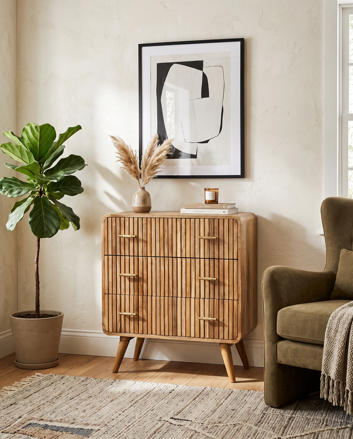 A ridged solid mango wood chest of drawers in a natural oak finish, styled in a cozy room setting with a potted fiddle leaf fig, an armchair, and framed art.