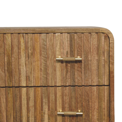 Close-up detail of a natural oak finish mango wood chest, showing the vertical ridged texture of the drawer front and a knurled brass bar handle.