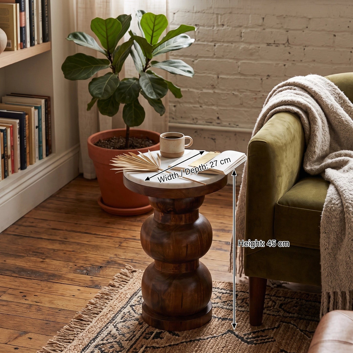 A round wooden, marble top end table with a carved pedestal base, shown in a cozy living room setting next to an olive green armchair. The table has dimension overlays indicating a width of 27 cm, a depth of 27 cm, and a height of 45 cm.