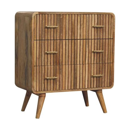 Angled right view of a three-drawer ridged solid mango wood chest in natural oak with mid-century style tapered legs.
