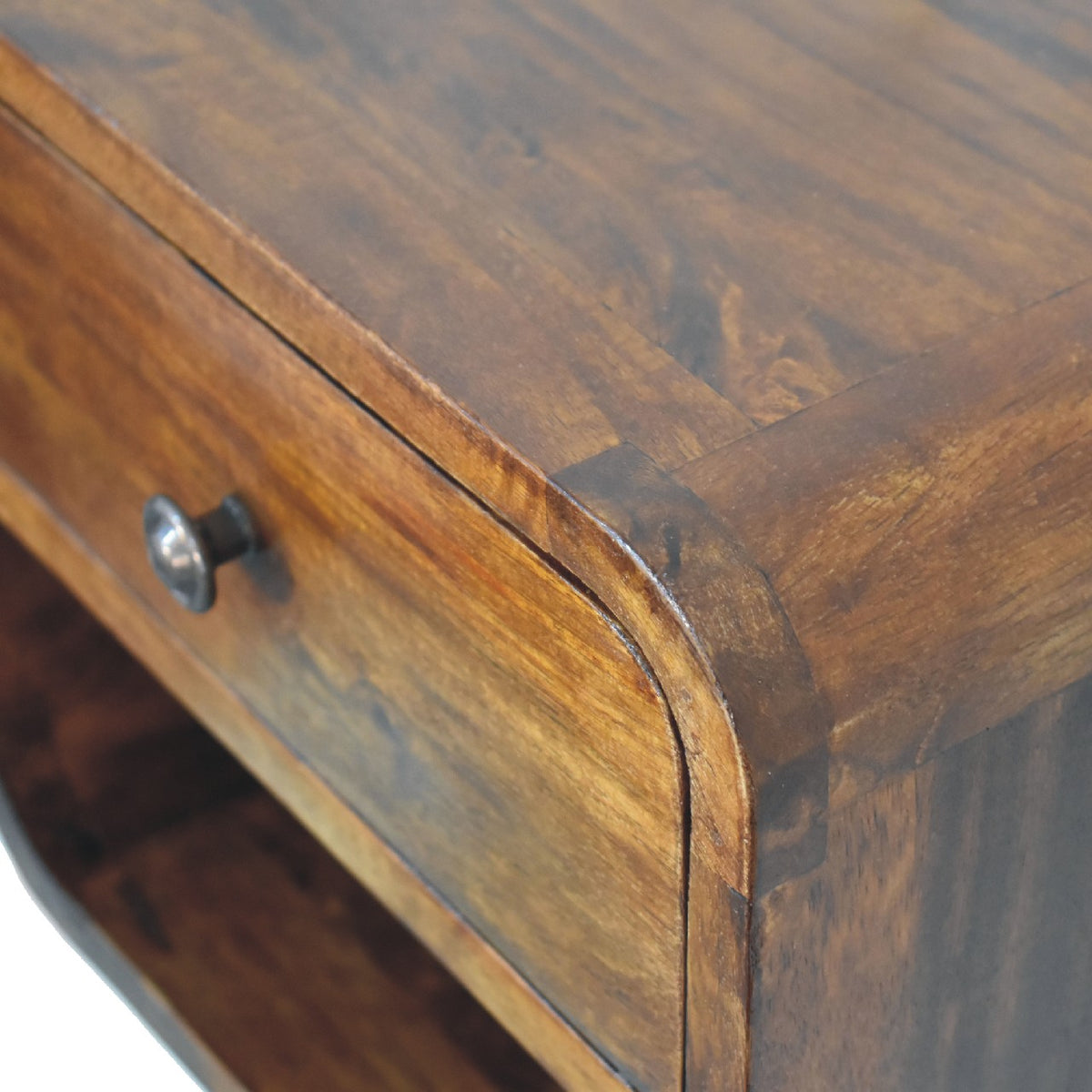 Detail shot focusing on the smooth rounded top corner and flush wood joinery of a curved floating bedside table in chestnut.