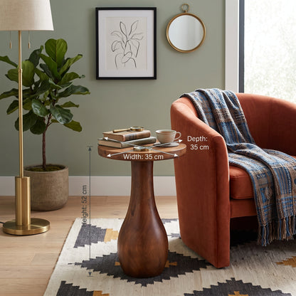 A wooden side table with a rounded pedestal base is shown in a styled living room setting next to an orange armchair, with dimension overlays indicating its width, depth, and height.