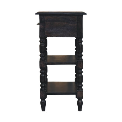 Straight-on side profile view of a solid mango wood 1-drawer side table in carbon ash, displaying its open shelves and turned leg silhouette.