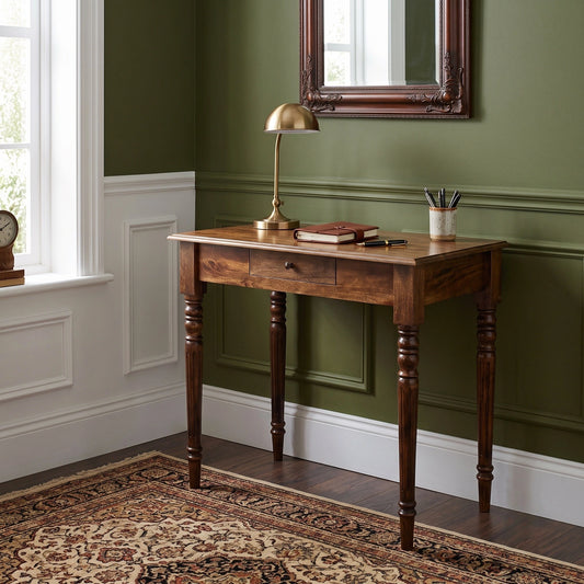 A dark brown wooden writing desk with a single drawer and turned legs, styled in a room with olive green paneled walls, white wainscoting, a patterned rug, and a brass desk lamp.