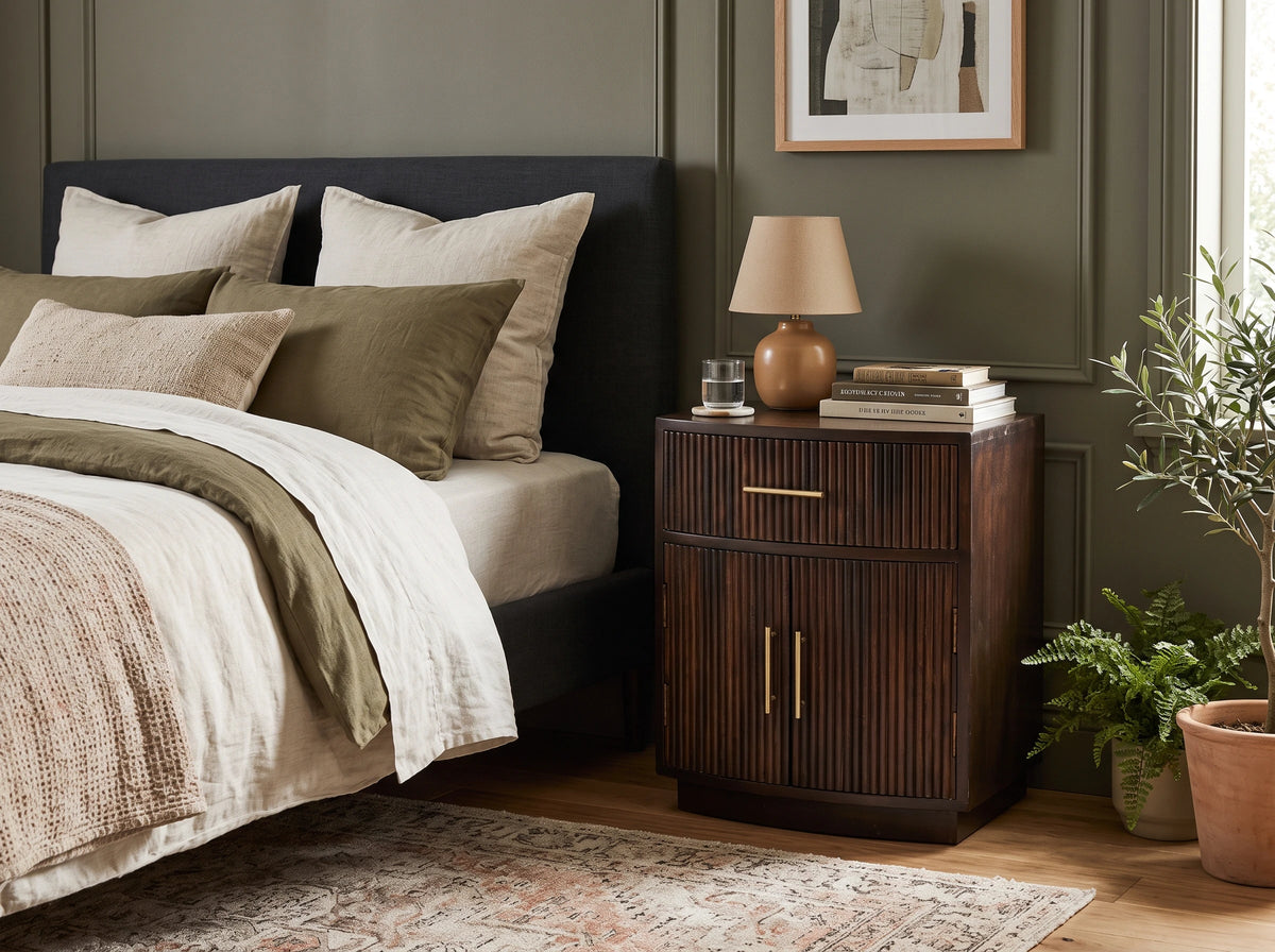 Lifestyle image of a velvet mocha solid mango wood fluted bedside table next to a bed. 
