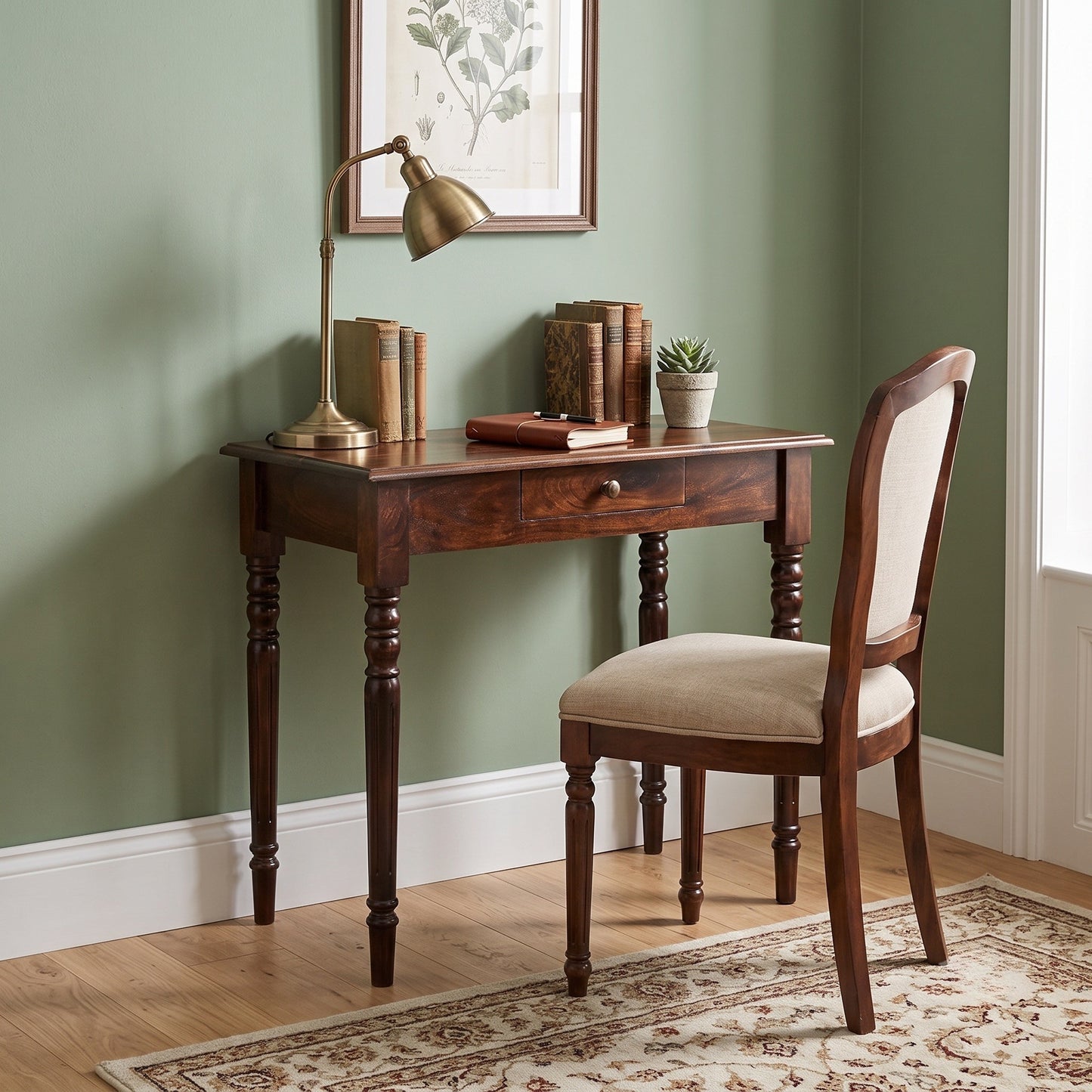 A dark brown wooden writing desk with a single drawer and turned legs, paired with a matching upholstered wooden chair in a styled room with sage green walls, a brass desk lamp, and books.